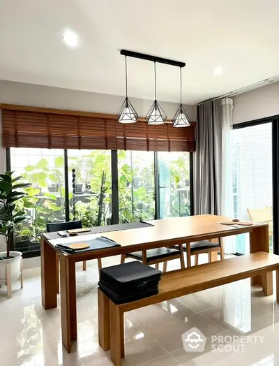 Spacious dining area with sleek wooden table, modern lighting, and a view of lush greenery through large windows, perfect for family gatherings.