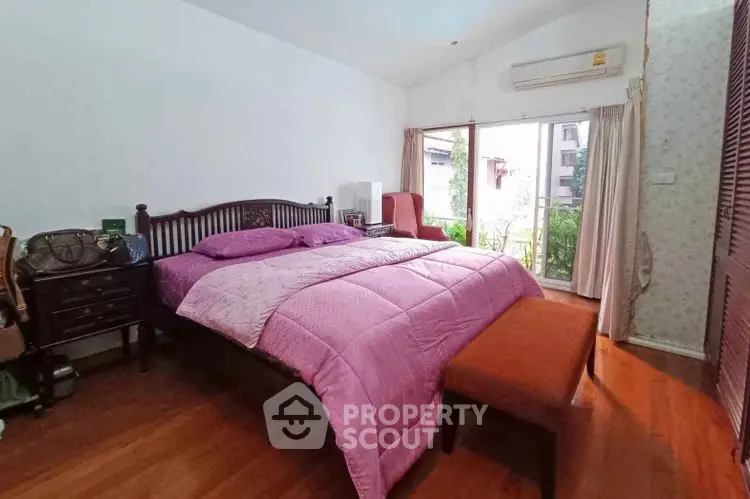 Cozy bedroom with wooden flooring and large window overlooking greenery.