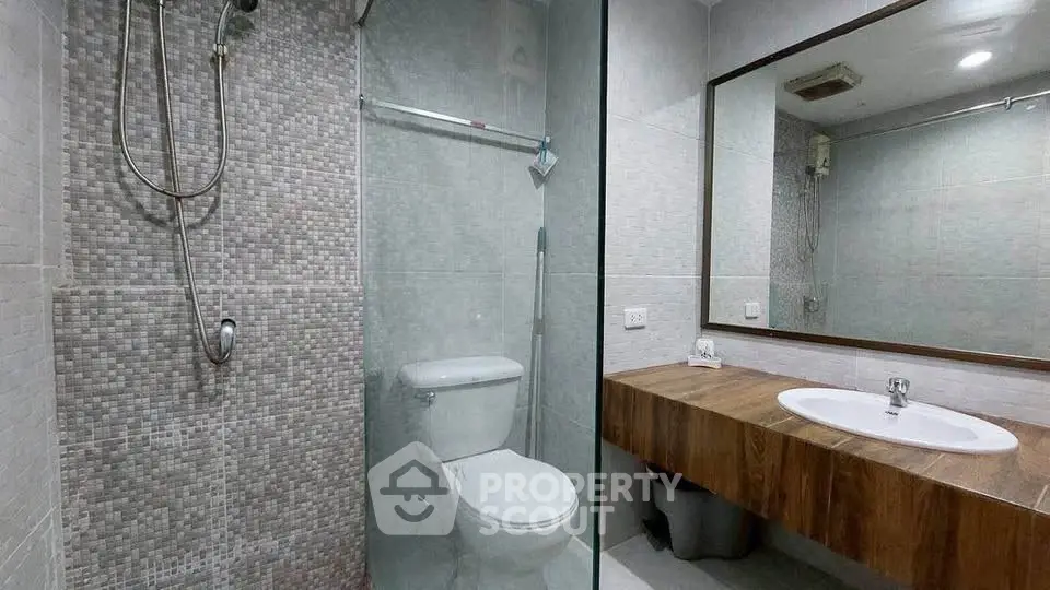 Modern bathroom with glass shower and wooden vanity in sleek apartment.