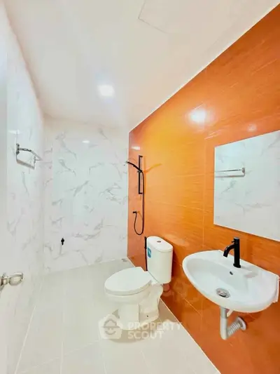 Modern bathroom with orange accent wall and sleek fixtures