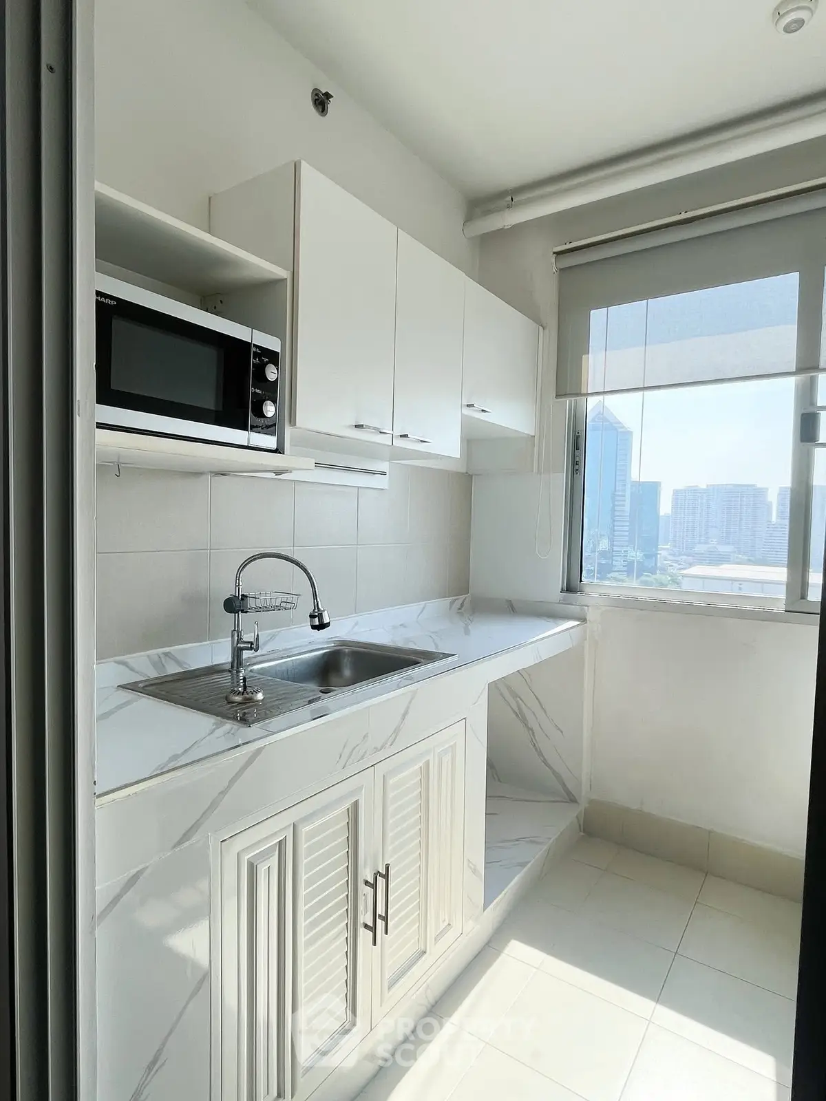 Modern kitchen with sleek cabinetry and city view, featuring a microwave and ample natural light.