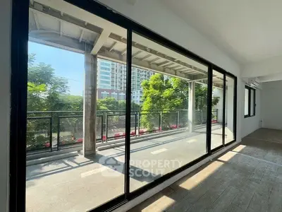 Spacious balcony with large glass doors offering a serene view of greenery and urban landscape.