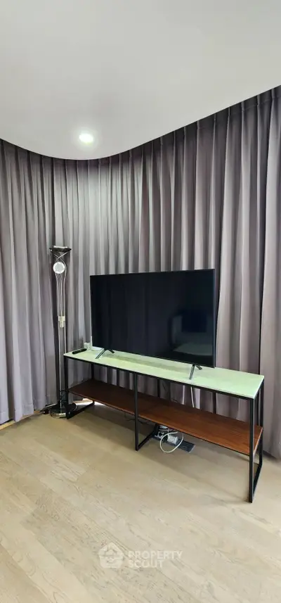 Modern living room with sleek TV stand and floor lamp, featuring elegant curtains and wooden flooring.