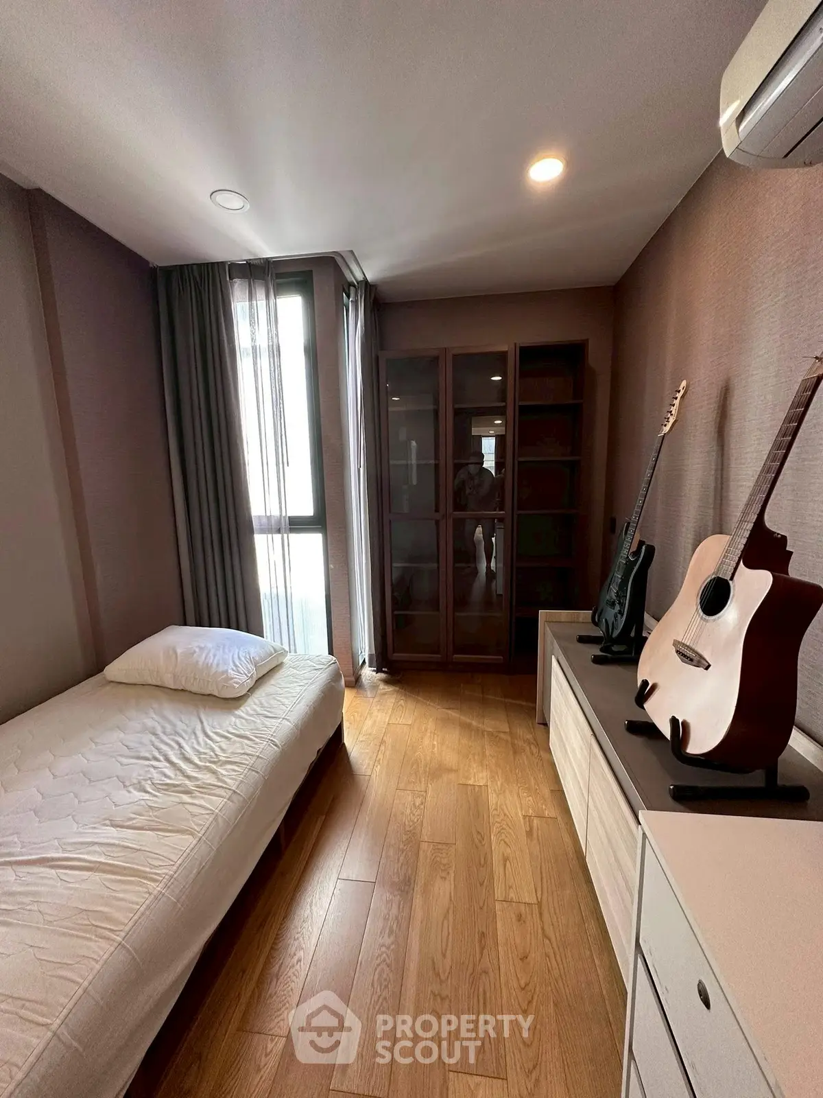 Cozy bedroom with wooden floor, single bed, and guitars, perfect for music lovers.