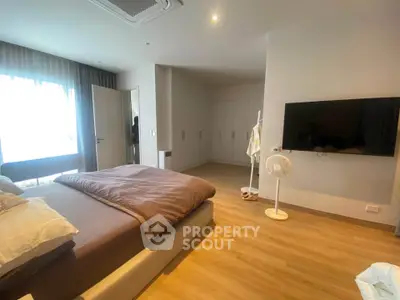Spacious modern bedroom with large window and wall-mounted TV, featuring elegant wooden flooring.
