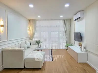 Elegant living room with modern decor, featuring a plush sofa, wall-mounted TV, and large window with sheer curtains.
