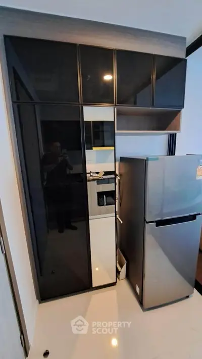 Modern kitchen with sleek black cabinets and stainless steel fridge in a compact layout.