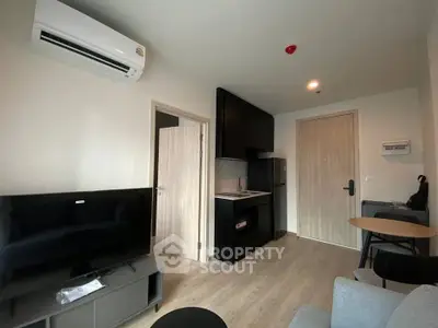 Modern apartment interior with compact kitchen and cozy living area, featuring sleek furniture and air conditioning.