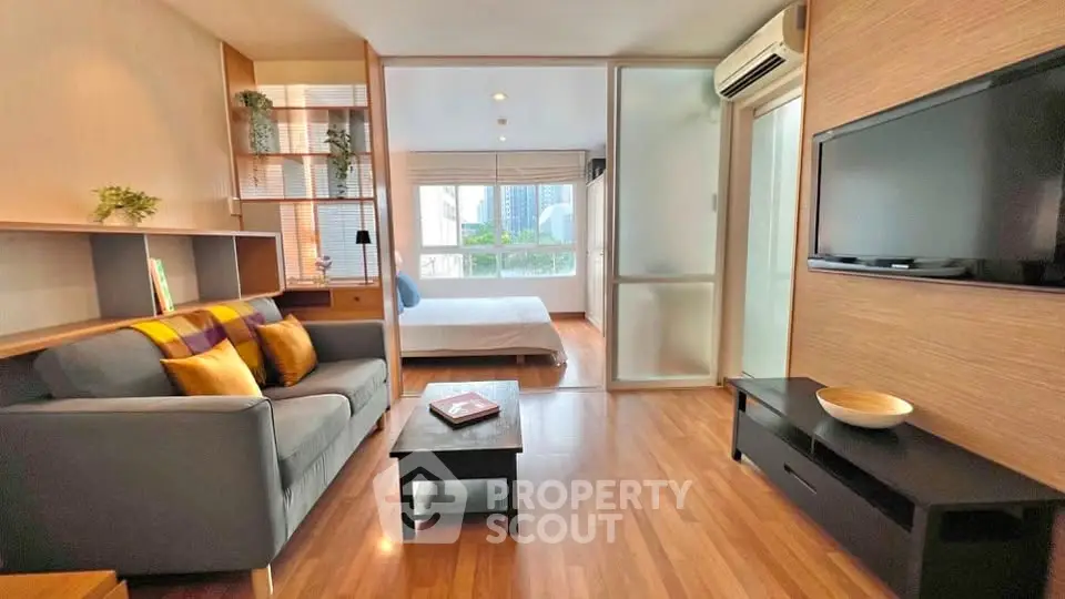Modern open-plan living room with cozy sofa, flat-screen TV, and view into a stylish bedroom.