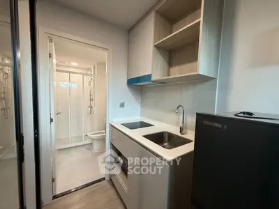 Compact modern kitchen with sleek appliances and adjacent bathroom in a stylish apartment.