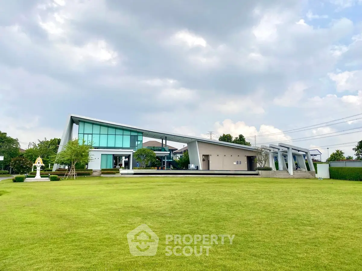Modern architectural building with sleek design and expansive green lawn under a cloudy sky.