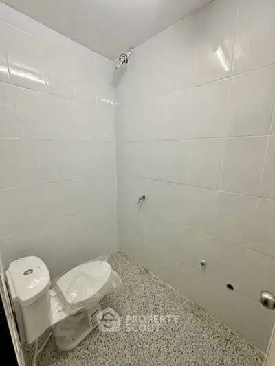 Minimalist bathroom with white tiled walls and basic fixtures, ideal for renovation.