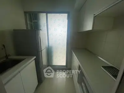 Compact modern kitchen with sleek white cabinetry and large fridge, featuring a frosted glass window for natural light.