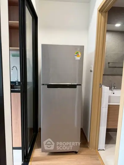 Modern kitchen with sleek stainless steel refrigerator and adjacent bathroom view.