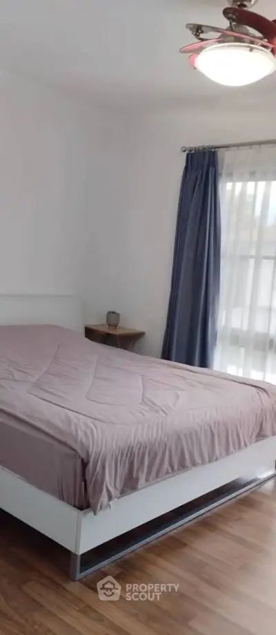 Spacious bedroom with modern decor and natural light, featuring a comfortable bed and elegant curtains.