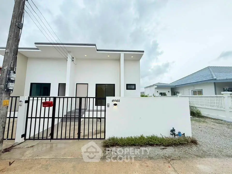 Modern minimalist white house with gated entrance and clean architectural lines.