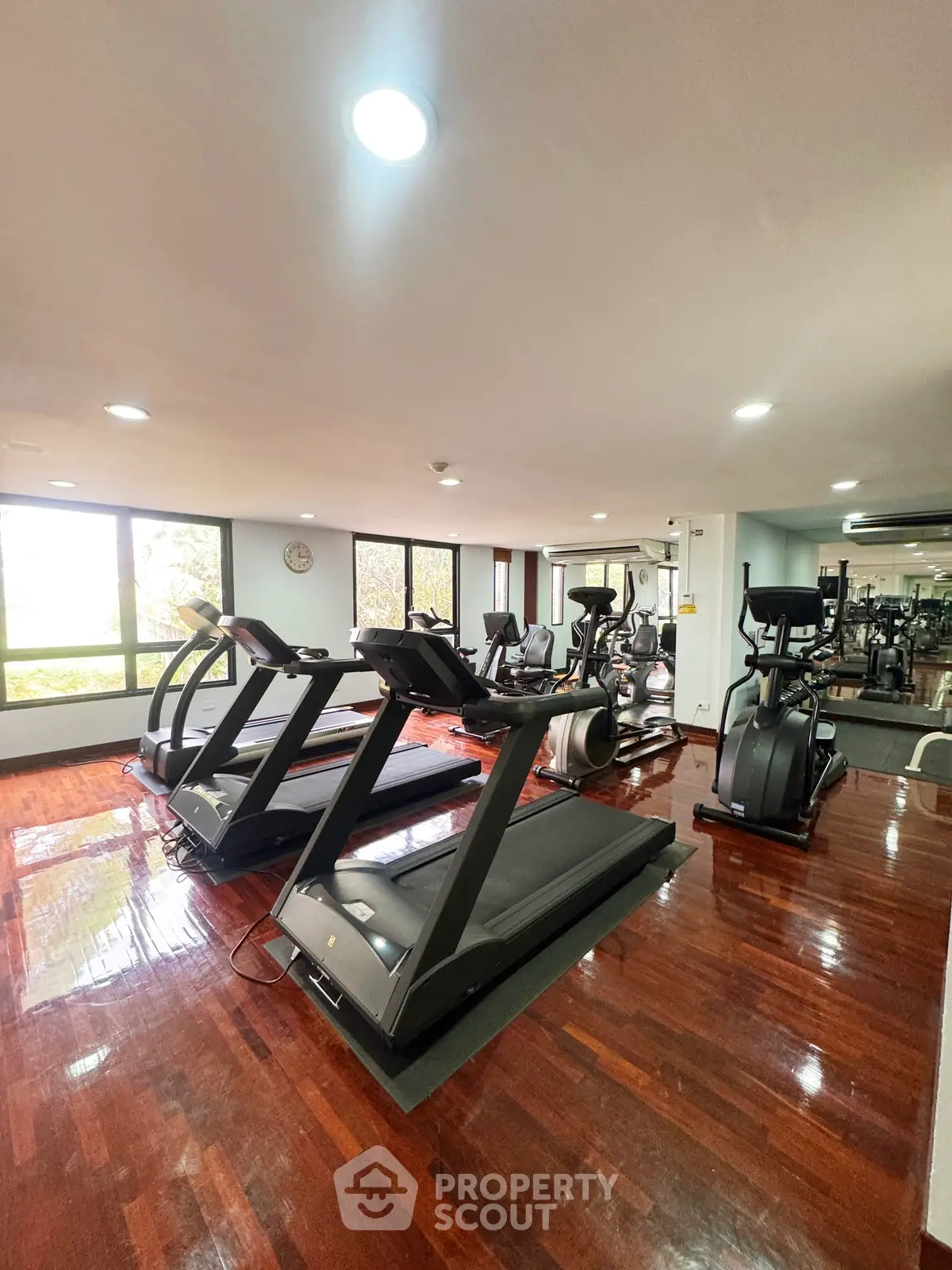 Spacious gym with modern equipment and polished wooden floors in a residential building.