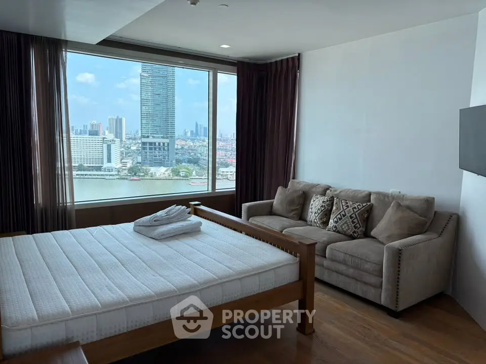 Spacious bedroom with stunning city and river view, featuring a cozy sofa and large window.