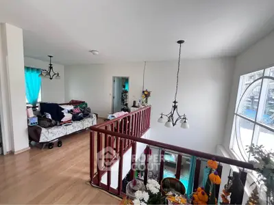 Spacious living area with wooden flooring and modern lighting, featuring a cozy seating arrangement and large windows.