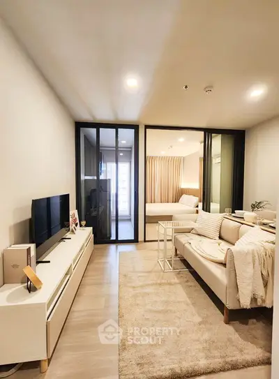 Modern living room with cozy sofa, TV unit, and sliding glass doors leading to bedroom.