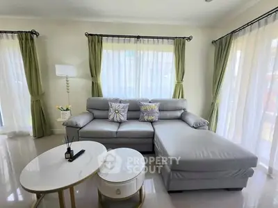 Spacious living room with elegant gray sofa and chic decor, featuring large windows with green curtains.