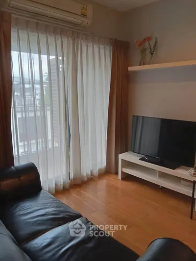 Cozy living room with leather sofa, TV, and large window with sheer curtains.