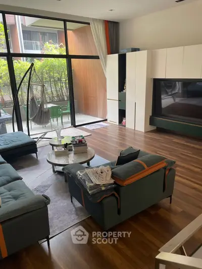 Spacious living room with modern furniture and large windows opening to a lush garden view.