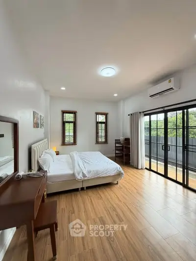 Spacious bedroom with large windows and balcony access, featuring modern decor and wooden flooring.