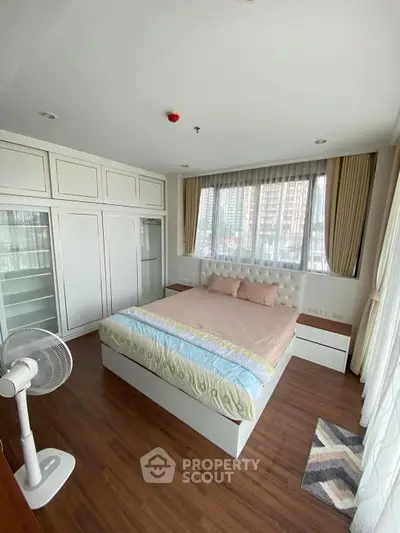 Spacious bedroom with large windows and modern furnishings in a high-rise apartment.