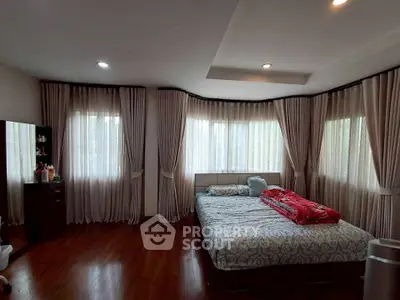 Spacious bedroom with large windows and elegant curtains, featuring a cozy bed and wooden flooring.