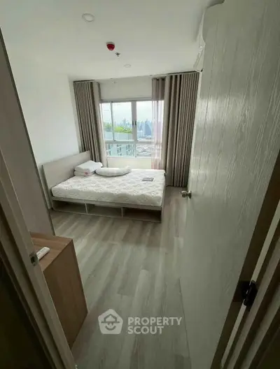 Modern bedroom with large window and city view, featuring minimalist decor and wooden flooring.
