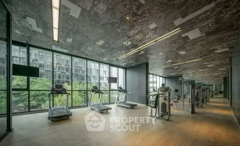 Modern gym with large windows and city view, featuring treadmills and exercise equipment.