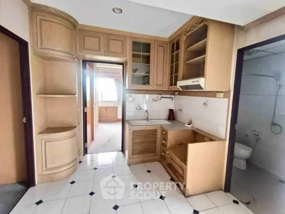 Charming compact kitchen with wooden cabinetry and tiled flooring, adjacent to a cozy bathroom.