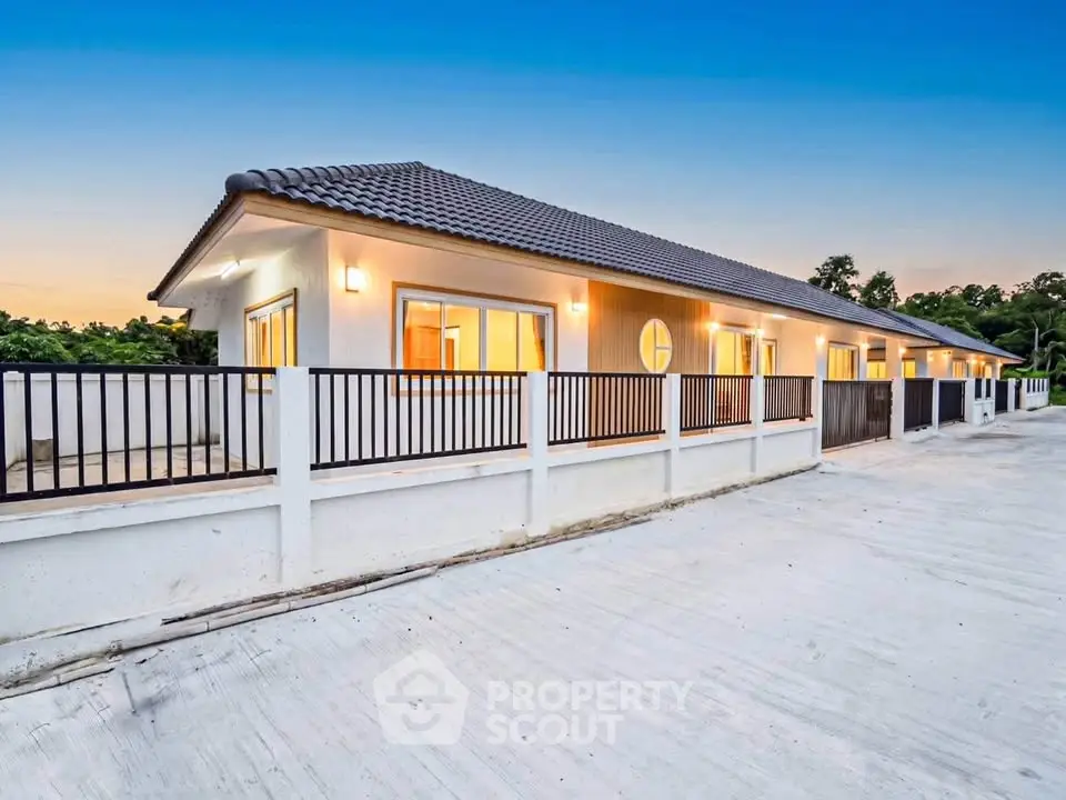 Modern single-story house with spacious balcony and elegant exterior lighting at sunset.