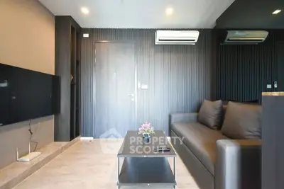 Modern living room with sleek black sofa and wall-mounted TV, featuring stylish decor and air conditioning.