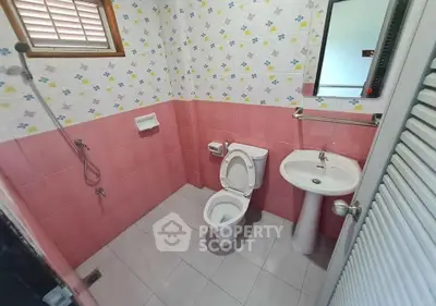 Charming bathroom with pink tiles and floral wallpaper, featuring a modern toilet and pedestal sink.