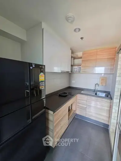 Modern kitchen with sleek black fridge and wooden cabinetry in a compact layout.