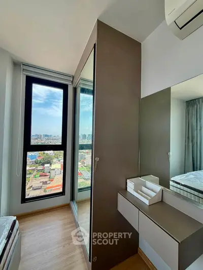 Modern bedroom with large window offering stunning city views, sleek mirrored wardrobe, and elegant wood flooring.