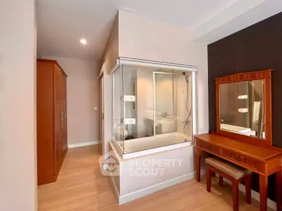 Modern bedroom with unique glass-enclosed bathtub and elegant wooden furniture.