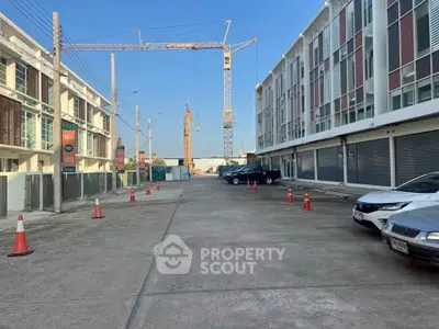 Modern commercial building exterior with parking area and construction crane in background.