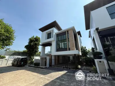 Modern three-story house with sleek design and large windows in a serene neighborhood.