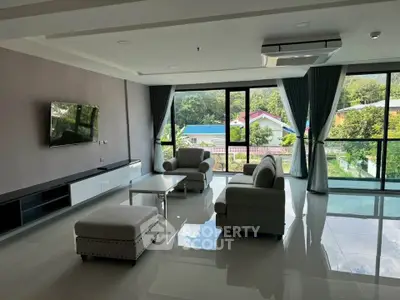 Spacious living room with large windows and modern furniture, offering a serene view of greenery.
