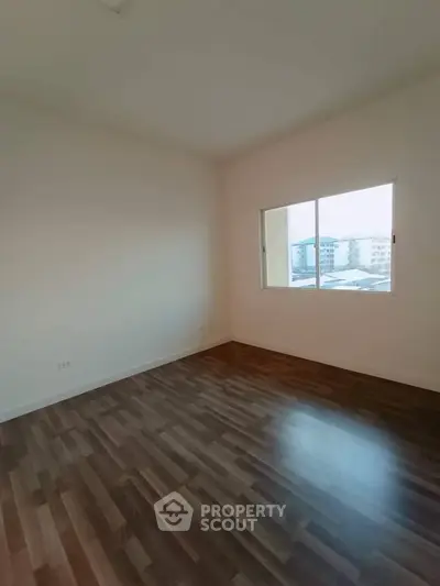 Spacious empty room with large window and wooden flooring, perfect for customization.