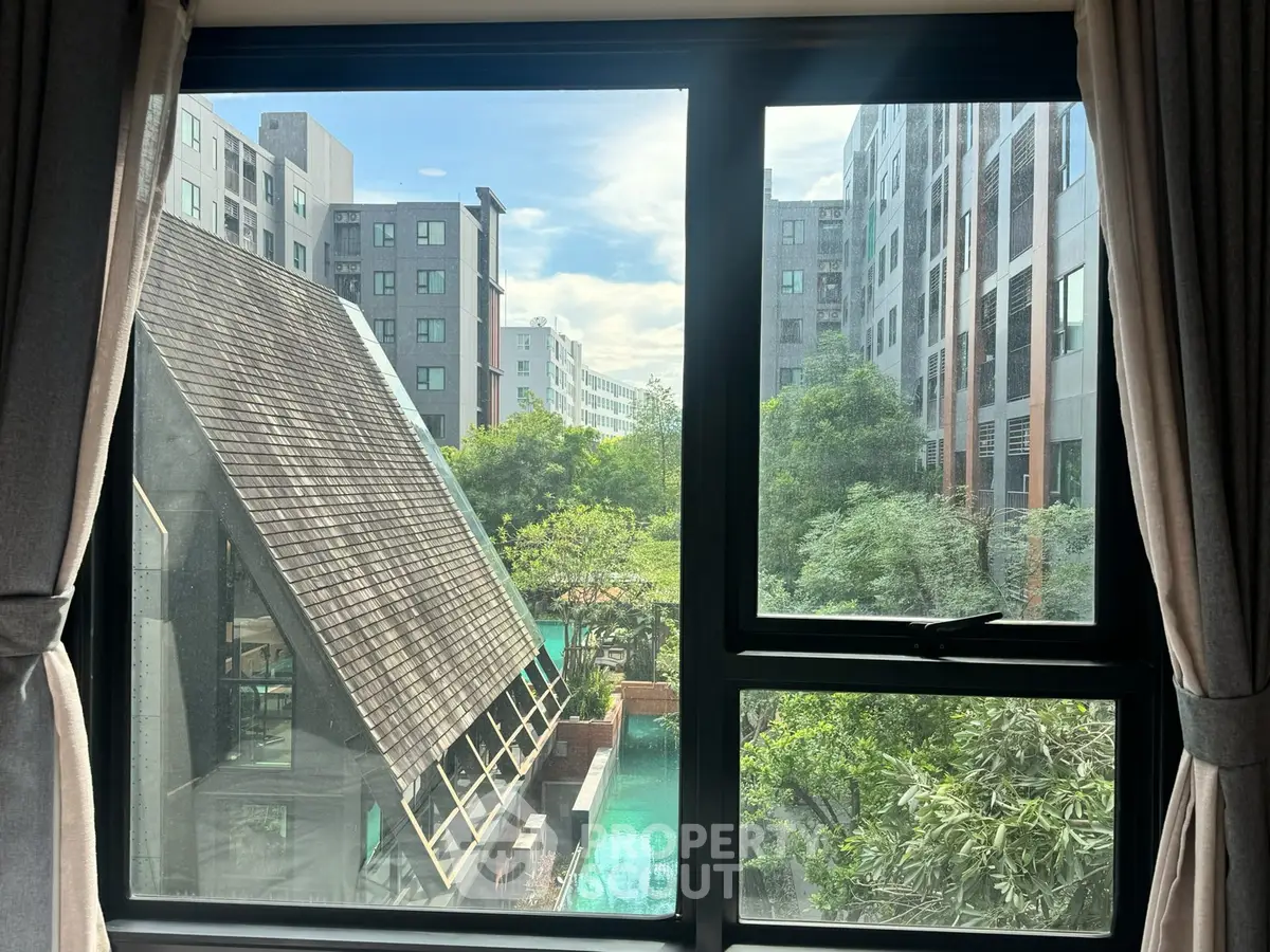 Stunning view from window overlooking modern architecture and lush greenery in urban setting.