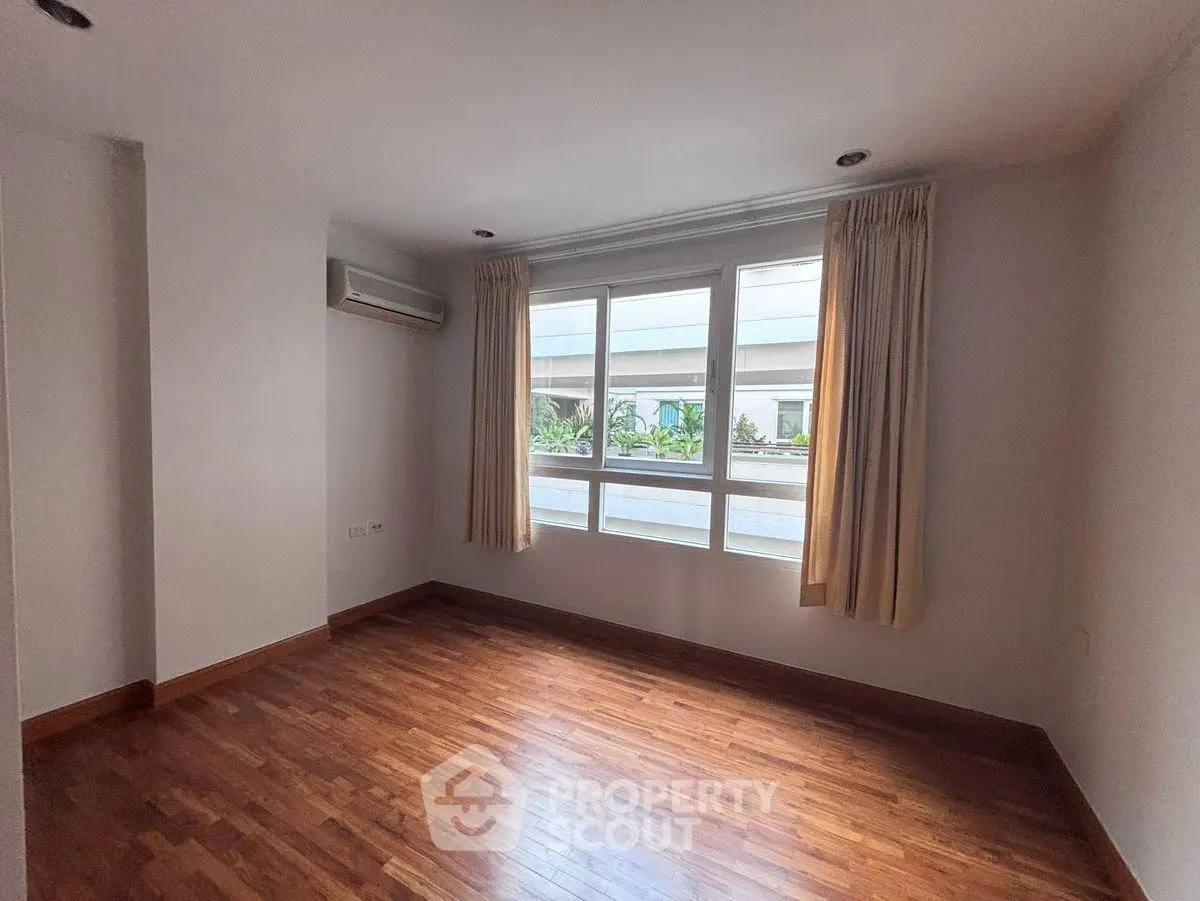 Spacious empty room with wooden flooring and large window in modern apartment.