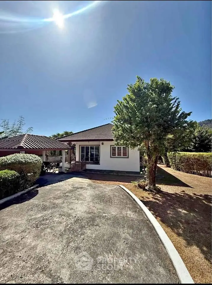 Charming single-story home with spacious driveway and lush greenery under a clear blue sky.