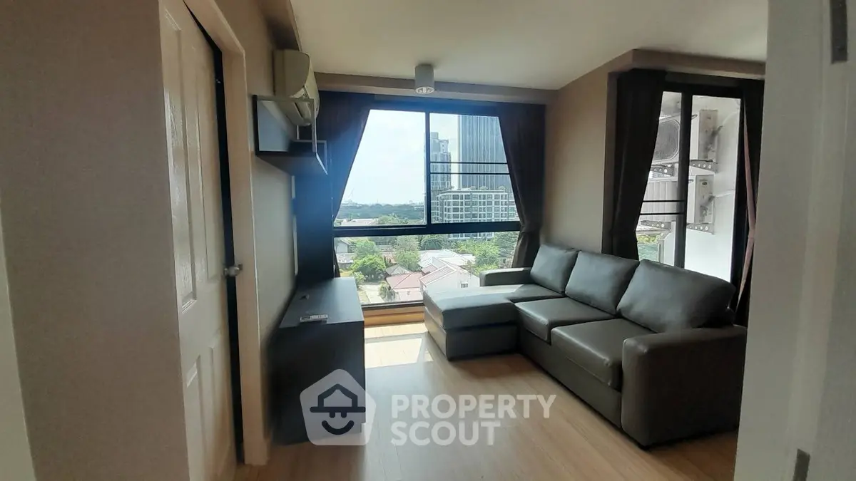 Modern living room with large windows and city view, featuring a sleek sofa and wooden flooring.