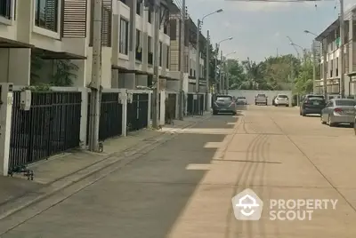 Modern townhouse street view with parked cars and lush greenery