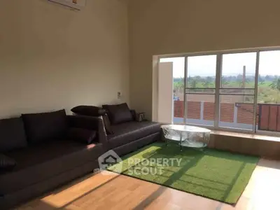 Spacious living room with large windows and modern furniture, offering a serene view.