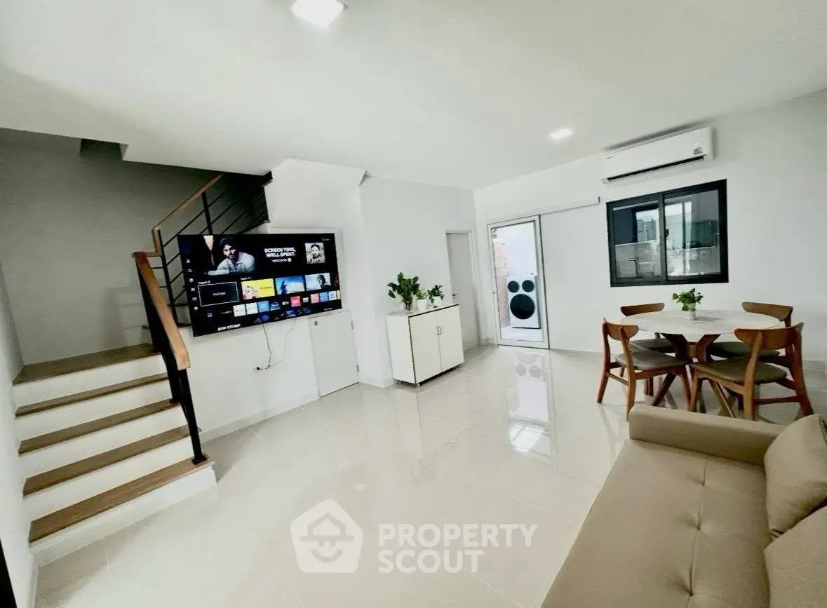 Modern living room with staircase, TV, dining area, and air conditioning in a bright open space.